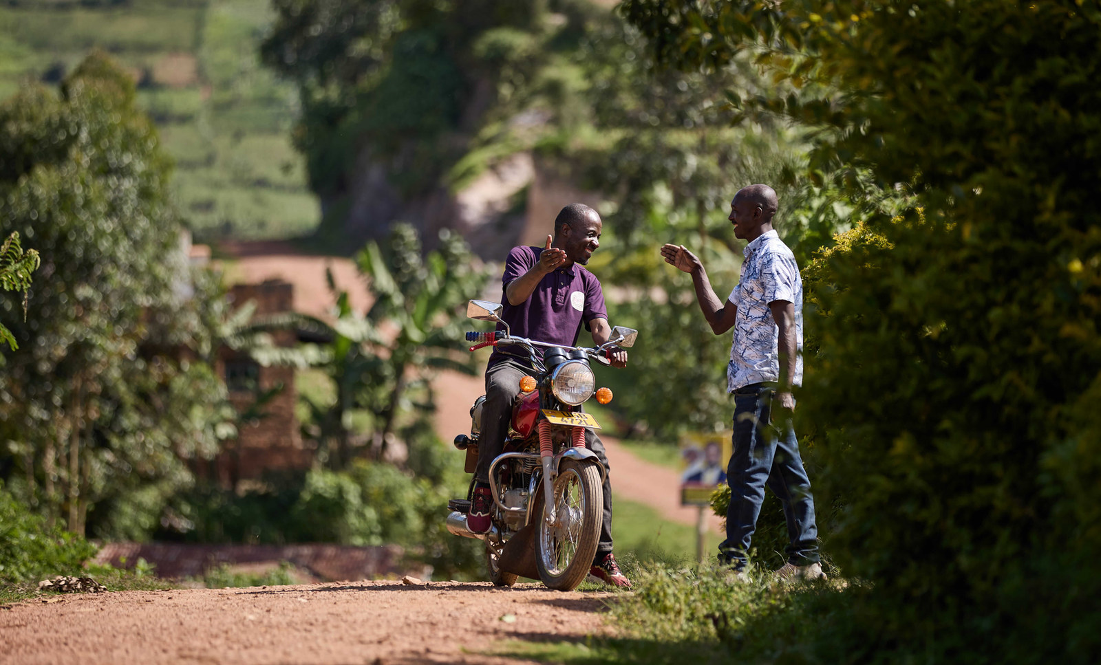 Two men talking beside a motorbike on a rural road
