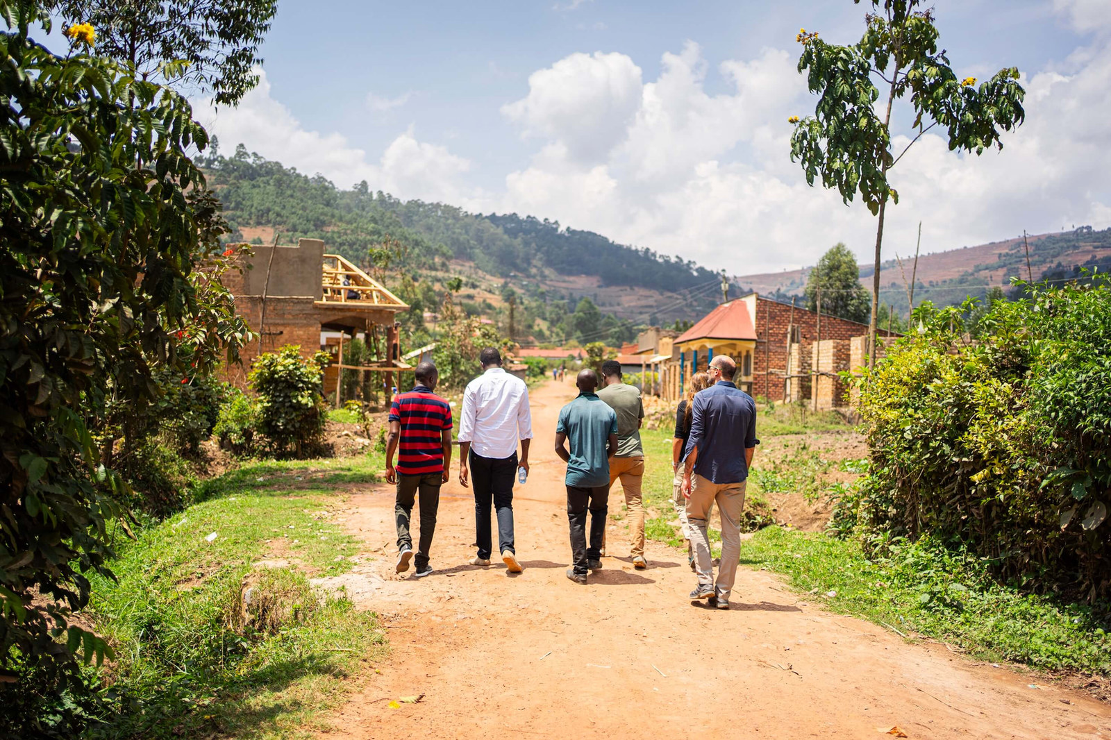 A group walking along a red dirt road between fields